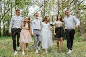 Casamento andar dentro a floresta. noivas e seus amigos pose contra a fundo do a floresta. uma ampla grupo do pessoas estão tendo Diversão às seus amigos' Casamento foto