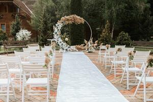 a Casamento arco dentro a parque é fez do fresco flores e seco juncos. longe Casamento cerimônia. branco cadeiras para a cerimônia foto