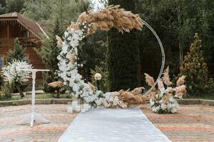 a Casamento arco dentro a parque é fez do fresco flores e seco juncos. longe Casamento cerimônia. branco cadeiras para a cerimônia foto