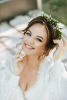 retrato do uma sorridente noiva em uma cama dentro a jardim debaixo uma árvore. a noiva é vestindo uma branco vestir e uma tiara do fresco flores em dela cabeça foto