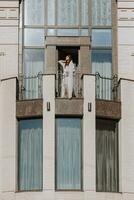 noiva em a sacada do a hotel dentro uma branco roupão com uma véu, livre espaço, vertical foto. em seu Casamento dia foto