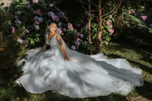 jovem lindo noiva dentro ombros caídos Casamento vestir perto hortênsia flores, moda foto ocupado debaixo suave luz solar
