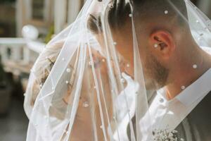 uma à moda casal do europeu recém-casados. sorridente noiva dentro uma branco vestir. a noivo, vestido dentro uma clássico Preto terno, branco camisa, debaixo uma véu. Casamento dentro natureza foto