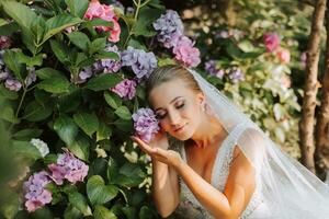 jovem lindo noiva dentro ombros caídos Casamento vestir perto hortênsia flores, moda foto ocupado debaixo suave luz solar