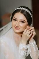 retrato do uma lindo jovem noiva dentro uma branco Casamento vestir com uma tiara em dela cabeça. final preparativos para a casamento. a noiva é esperando para a noivo. manhã, noiva. foto