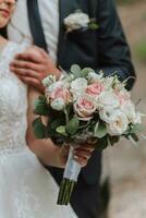 uma Casamento ramalhete do branco e Rosa rosas dentro a mãos do a noiva. fechar-se foto do a ramalhete