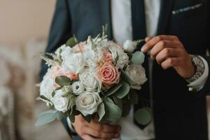 confiante elegante bonito cara dentro uma agradável Sombrio azul terno com uma ramalhete do flores dentro dele mãos. a noivo é preparando para a Casamento cerimônia foto