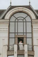 noiva em a sacada do a hotel dentro uma branco roupão com uma véu, livre espaço, vertical foto. em seu Casamento dia foto