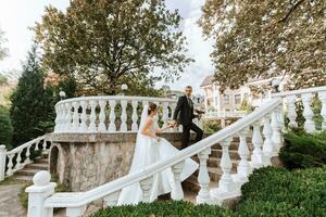 retrato do uma jovem noiva dentro uma branco vestir e uma morena noivo dentro uma terno caminhando baixa a passos do a velho cidade parque. uma lindo e romântico casamento, uma feliz casal foto