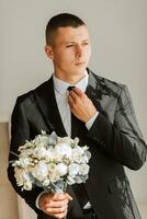 à moda noivo com uma ramalhete do flores dentro uma hotel sala. do noivo manhã. a noivo é obtendo pronto dentro a manhã antes a Casamento cerimônia foto