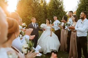 Largo ângulo tiro do noiva e noivo caminhando baixa a corredor depois de seus Casamento cerimônia às pôr do sol Como amigos e família comemoro foto