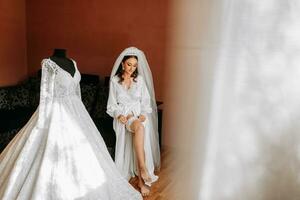 mulher vestindo uma liga em a perna. a noiva detém dentro mão perder liga dentro hotel sala. manhã preparação Casamento conceito. foto