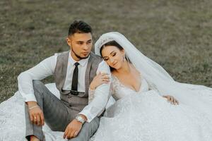 elegante noivo e fofa morena noiva dentro branco vestir com coroa, abraçando, rindo dentro parque, jardim, ao ar livre. Casamento fotografia, retrato do sorridente recém-casados. foto