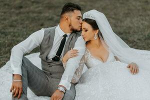 elegante noivo e fofa morena noiva dentro branco vestir com coroa, abraçando, rindo dentro parque, jardim, ao ar livre. Casamento fotografia, retrato do sorridente recém-casados. foto