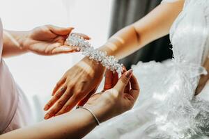 Casamento tema. uma amigo coloca uma pulseira em a noiva. a último minutos do preparativos para a casamento. mesmo roupa. feito à mão joalheria foto