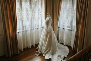uma luxuoso renda Casamento vestir dentro a caro interior do uma hotel iluminado de natural luz a partir de uma janela em dois lados foto