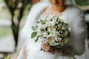 uma lindo rainha com uma ramalhete do flores dentro dela mãos. encantador mulher noiva é caminhando dentro a parque. uma Casamento roupa, uma exuberante vestir, uma luxuoso capa, uma branco capa fez do cisne penas. foto