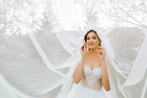 fechar-se tiro do a elegante morena noiva dentro uma branco vestir posando debaixo uma véu fechar-se. noiva retrato, Casamento Maquiagem e Penteado, nupcial moda. lindo noiva dentro uma véu foto