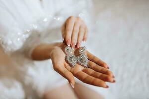 Casamento brincos em uma mulher mão, ela leva brincos, elegante da noiva brincos, manhã noiva, branco vestir, vestindo brincos foto