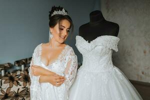 uma feliz noiva é preparando para dela luxuoso Casamento às lar, segurando dela lindo vestir dentro dela mãos. retrato do uma mulher com profissional cabelo e Maquiagem e uma sorrir dentro uma roupão de banho foto