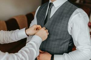 a noivo é preparando para a cerimônia. amigos Socorro a noivo preparar para a casamento. a homem coloca em uma terno e prepara para a encontro foto