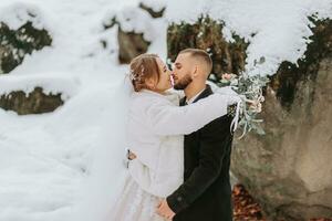 Casamento dentro inverno. a noiva e noivo estão em pé contra a fundo do coberto de neve pedras. anda em entre pedras e ampla pedras dentro a floresta foto