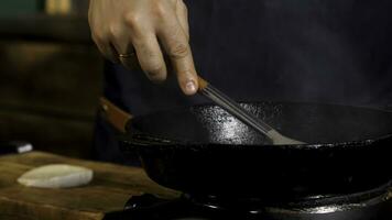 fechar acima do masculino cozinhar fritar molho e adicionando açúcar ou sal dentro uma Preto ferro frigideira. estoque imagens de vídeo. processo do Comida preparação às a restaurante. foto