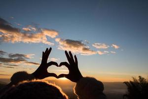 silhueta de mãos formando um coração com o nascer do sol foto