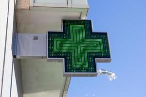 farmácia sinal elétrico na fachada do edifício. cruz verde iluminada foto