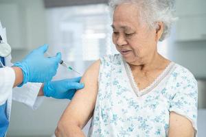 mulher idosa asiática sênior usando máscara facial recebendo vacina de covid-19 ou coronavírus pelo médico fazer injeção. foto
