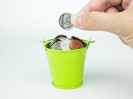 economizando moedas em um balde verde sobre fundo branco, conceito de negócio foto