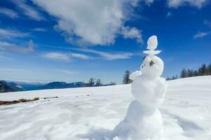 pequeno boneco de neve em uma Nevado montanha com azul céu durante caminhada foto