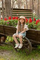 pré-adolescente menina sentado em roda do rústico de madeira carrinho usava Como flor cama dentro cidade parque foto