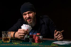 barbudo homem com charuto e vidro sentado às pôquer mesa e gritando isolado em Preto foto
