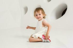 sorridente pequeno menina sentado em a chão em uma branco fundo foto