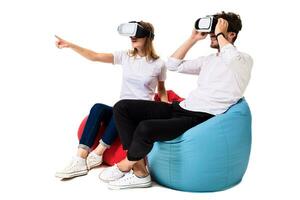 animado jovem casal experimentando virtual realidade sentado em pufes isolado em branco fundo foto