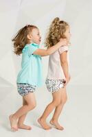 dois pequeno engraçado e rindo menina dentro a idêntico roupas do diferente cores jogando dentro branco estúdio foto