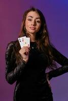 morena mulher dentro Preto veludo vestir mostrando dois jogando cartões, posando contra coloful fundo. jogos de azar entretenimento, pôquer, casino. fechar-se. foto