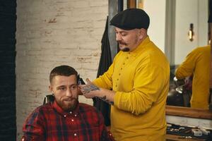 barbeiro fazendo corte de cabelo de atraente homem barbudo na barbearia foto