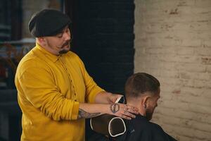 barbeiro fazendo corte de cabelo de atraente homem barbudo na barbearia foto