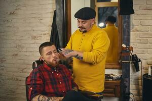 barbeiro fazendo corte de cabelo de atraente homem barbudo na barbearia foto