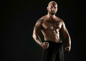 Atlético Careca, barbudo, tatuado homem dentro Preto calção é posando contra uma Preto fundo. fechar-se retrato. foto