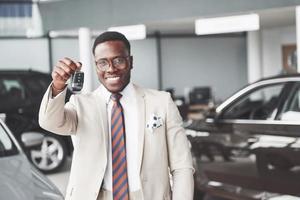 o jovem empresário negro e atraente compra um carro novo, ele tem as chaves na mão. sonhos se tornam realidade foto