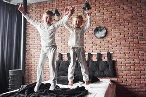 crianças travessas menino e menina encenaram uma guerra de travesseiros na cama do quarto. eles gostam desse tipo de jogo foto