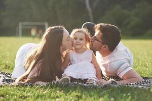 mãe e pai passam tempo juntos felizes. filha brinca com os pais ao ar livre durante o pôr do sol foto