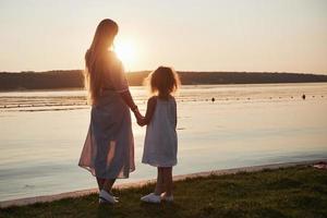 mãe brinca com seu bebê nas férias perto do mar, silhuetas ao pôr do sol foto