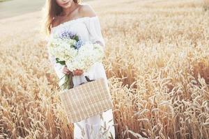 jovem sensível em um vestido branco posando em um campo de trigo dourado