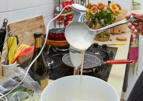 caseiro cozinha anfitriã derramando panqueca misturar a partir de concha para dentro vazando tigela foto