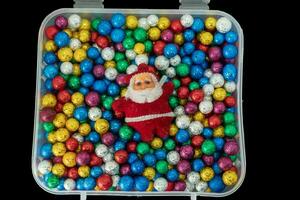santa claus com pilha do pequeno colorida termocol bolas dentro plástico caixa isolado em Preto fundo. foto