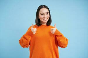 Boa trabalho. sorridente coreano mulher mostra polegares acima dentro aprovação, gostar smth, dá Boa opinião, acena com a cabeça dentro positivo responder, recomenda algo, azul fundo foto